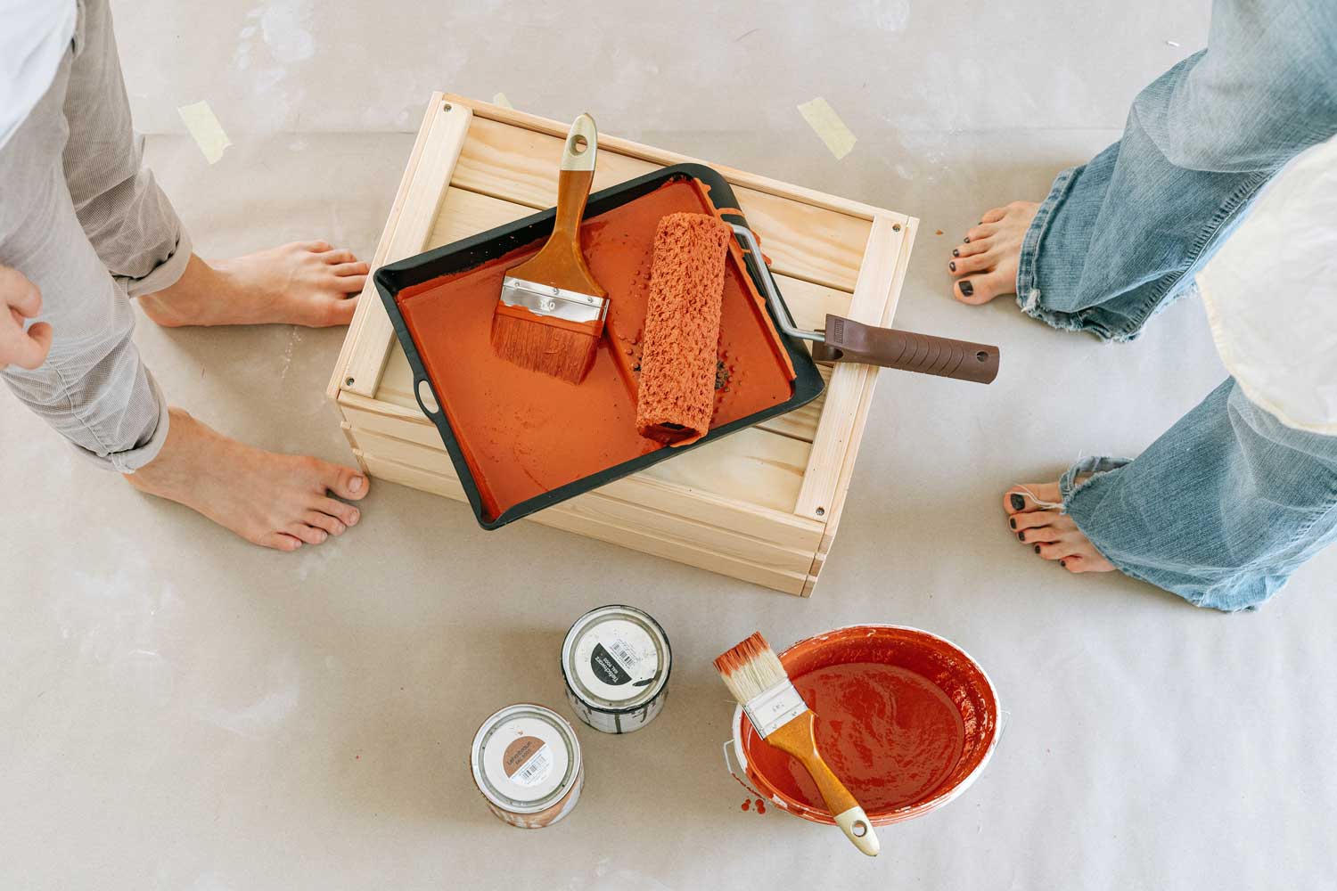 Couple painting home interior with orange paint bucket and paintbrushes