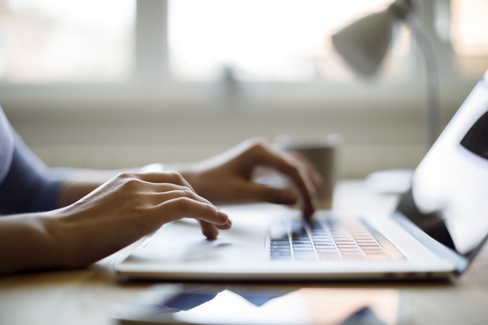 Close-up of hands typing on a laptop keyboard looking up resources 