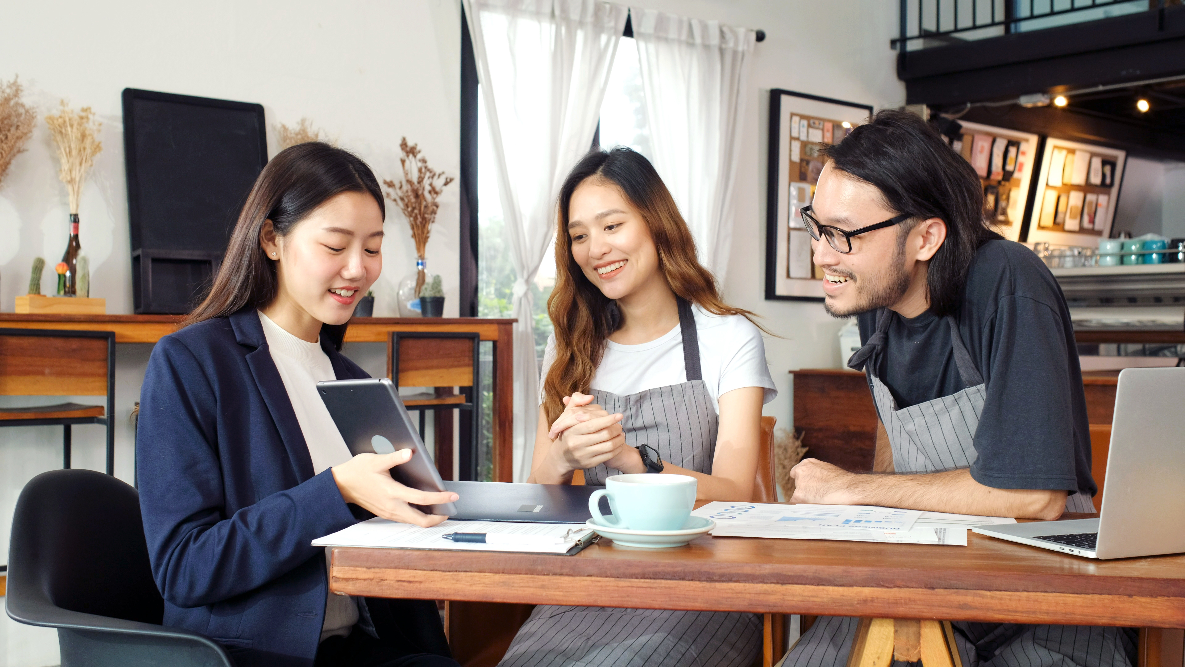 Small Business owners sitting at table with a professional woman, looking at her tablet.