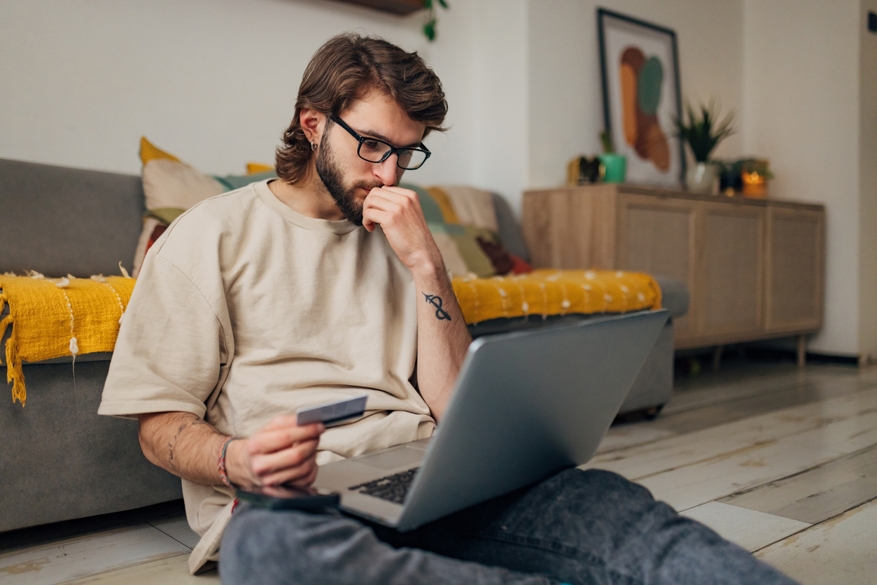 Man holding a credit card while looking at a laptop