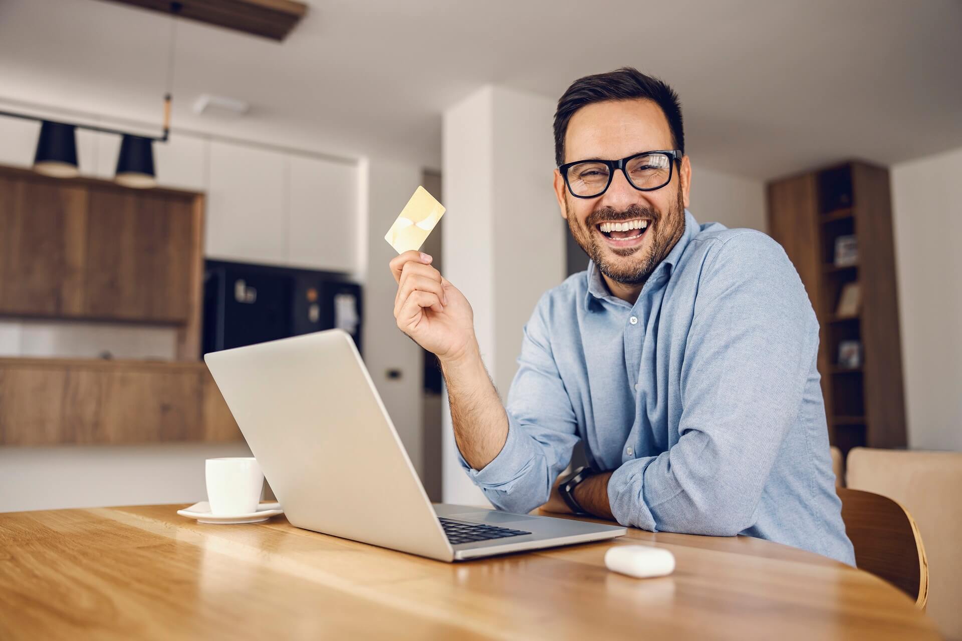 Smiling credit union member holding a debit card while working on a laptop at a desk representing checking accounts 