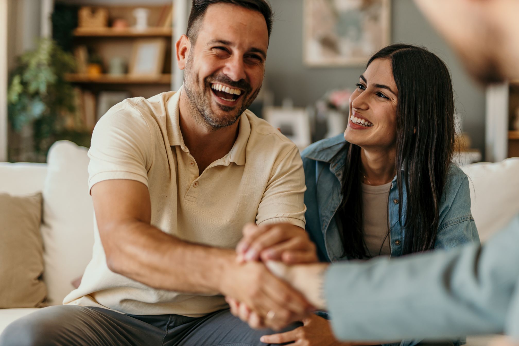 Young happy couple on a couch, man shaking hands with someone out of frame in front of him