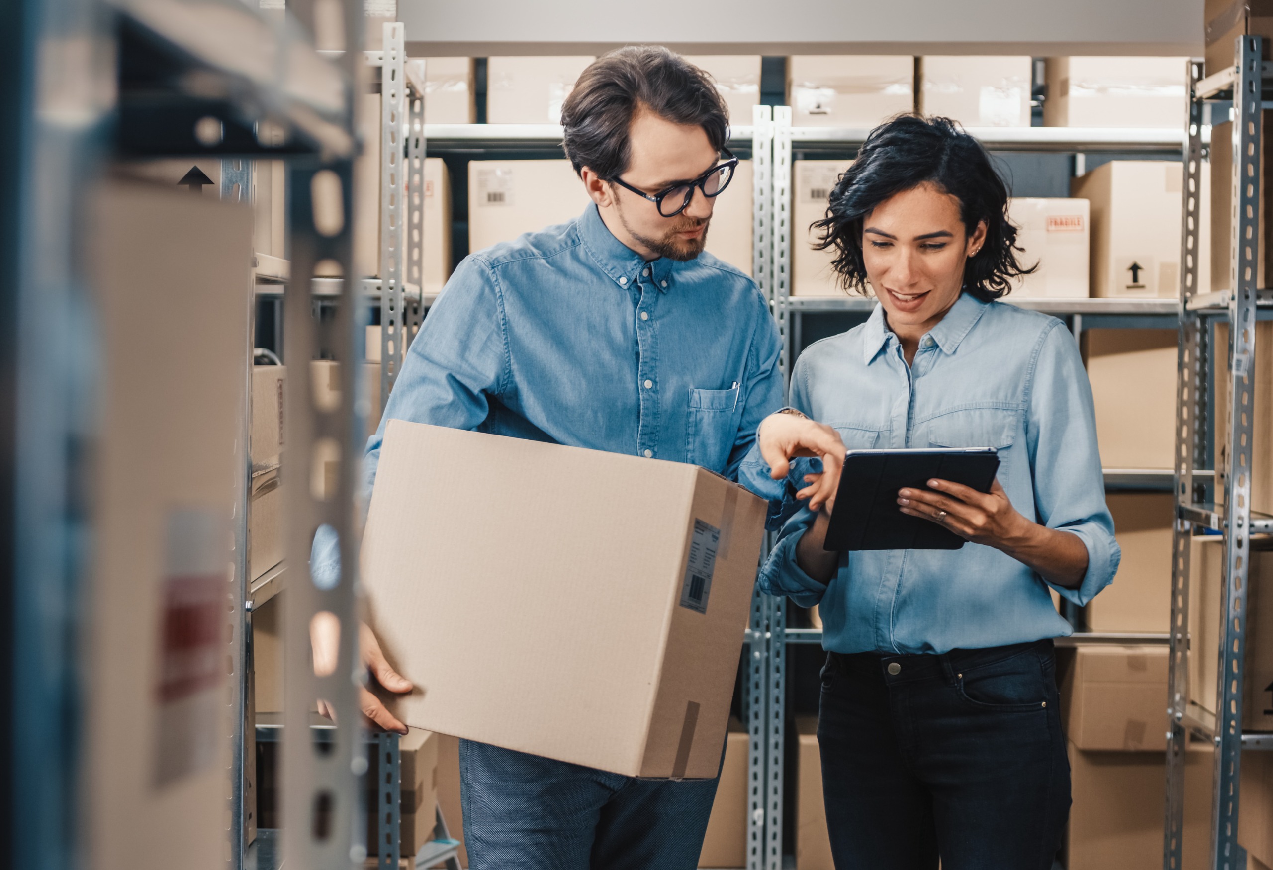 Man holding box and women holding tablet in a warehouse storage area