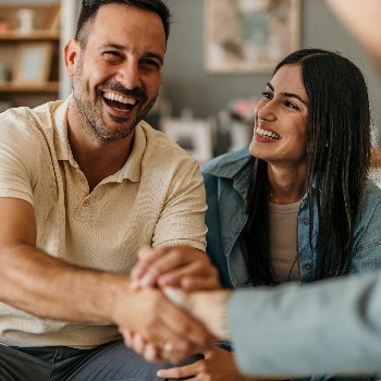 Young happy couple on a couch, man shaking hands with someone out of frame in front of him