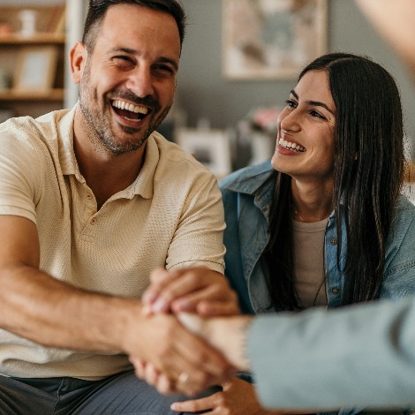 Young happy couple on a couch, man shaking hands with someone out of frame in front of him