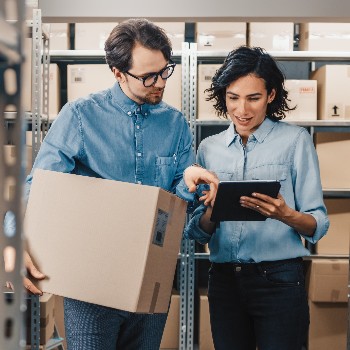 Man holding box and women holding tablet in a warehouse storage area