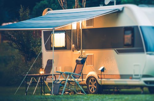 RV Parked on Grass at Night With Two Chairs Outside 