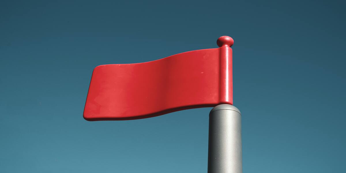The image depicts a vibrant red flag against a clear blue sky.